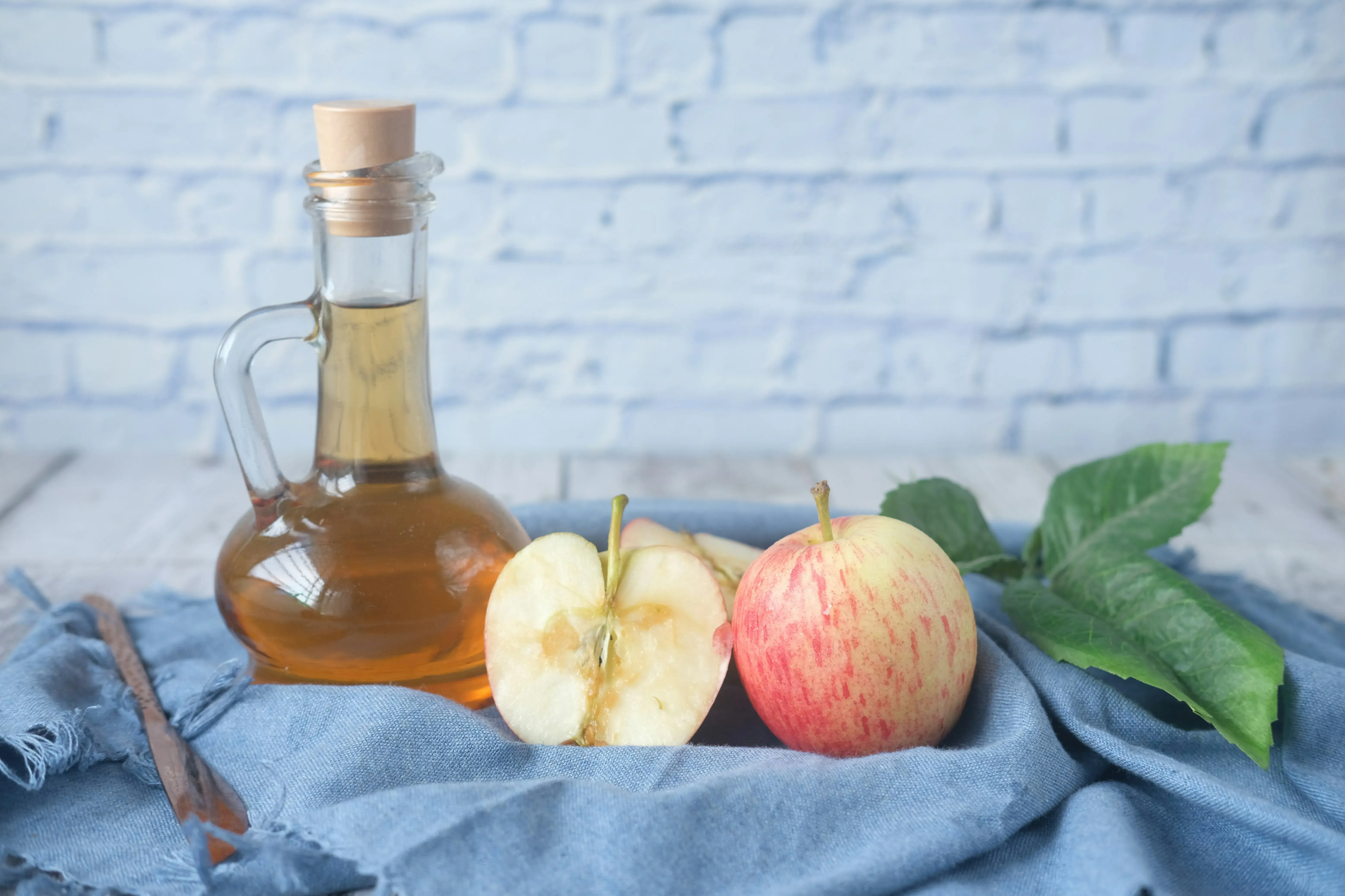 bottle of vinegar next to two apples. One of the apples is sliced in half to see the inside.