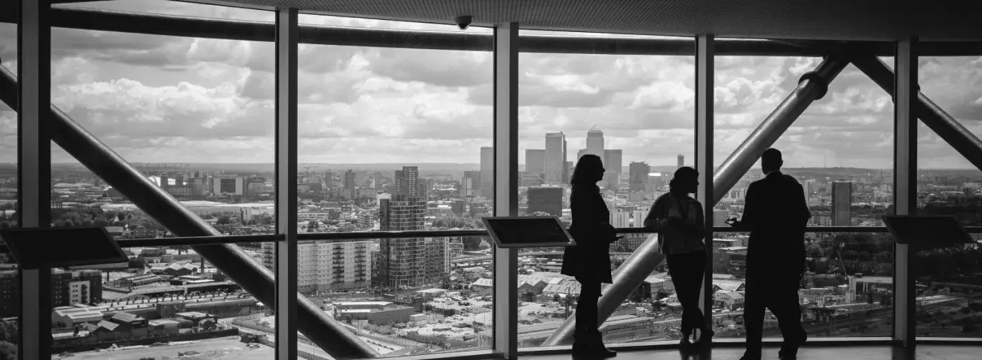 black and white photo of three people talking in front of a large panoramic window overlooking the city.