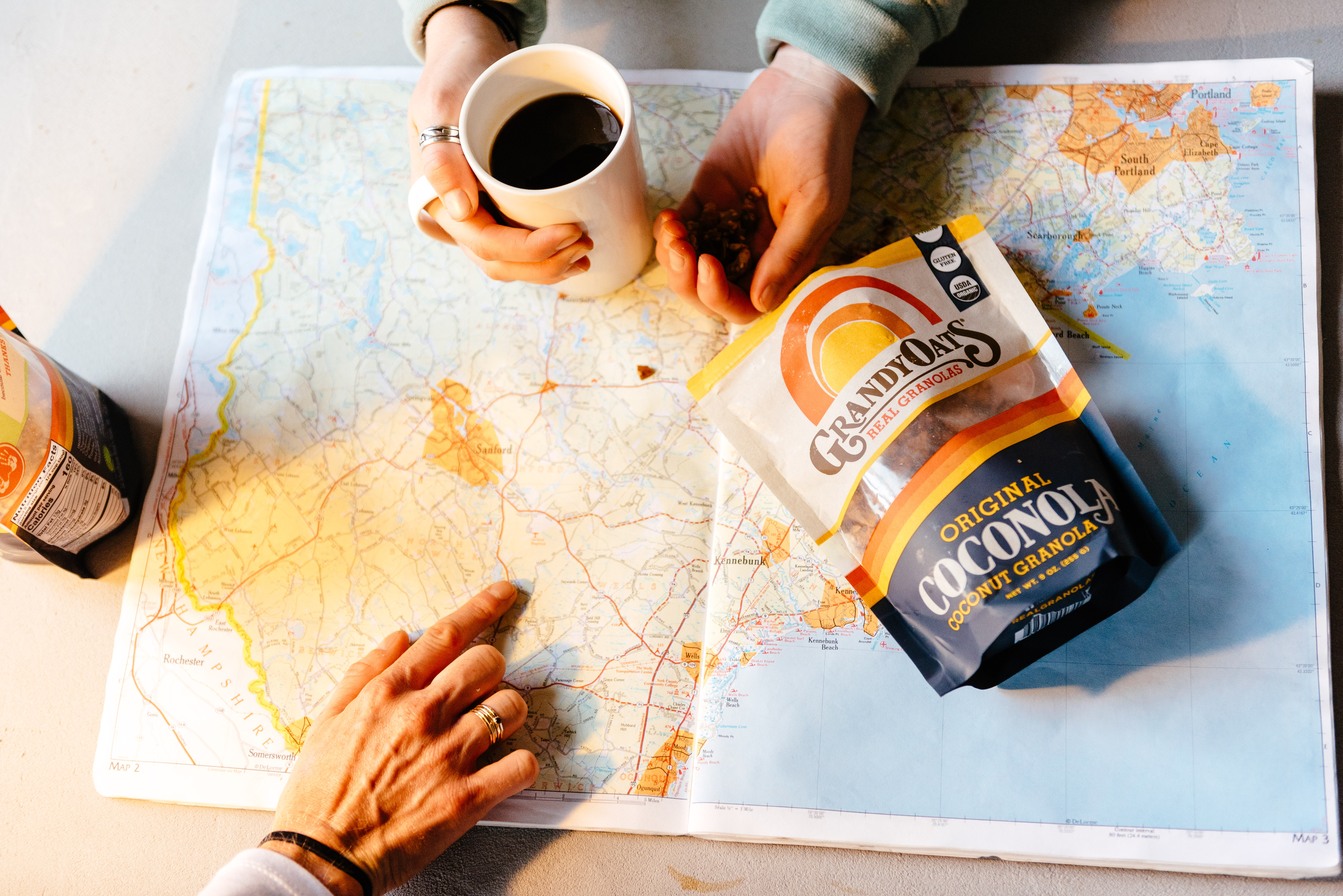 Two sets of hands, coffee, and GrandyOats granola on top of a map