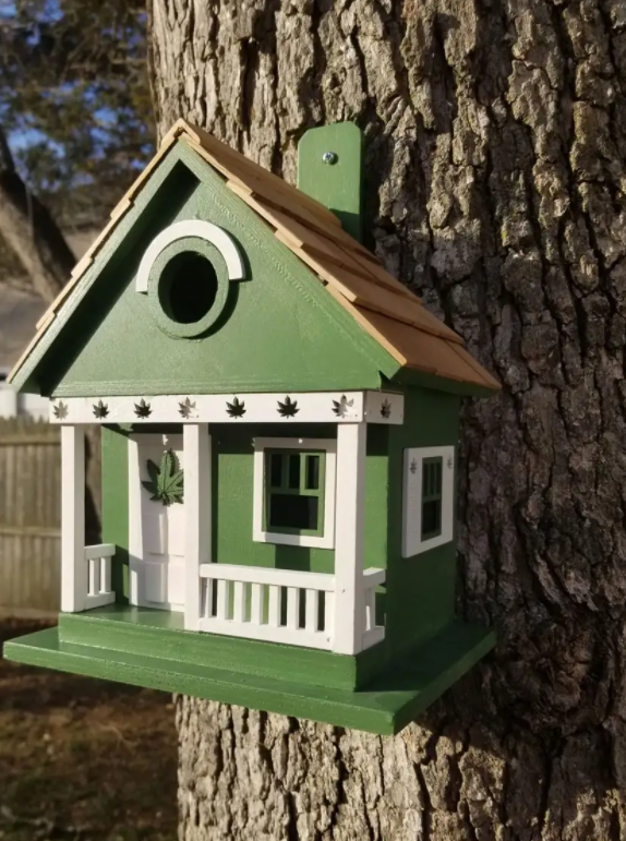 green bird house shaped like the front of a cottage with marijuana plants on it