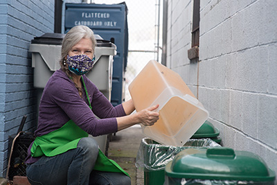 woman empties bucket into compost bin in an alley