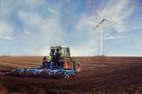 Image: tractor on a field with a wind turbine. Topic: Regenerative Agriculture.