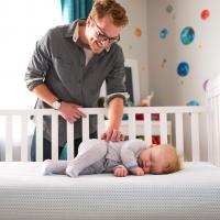 Image: father smiling over baby in crib. Organic baby products.