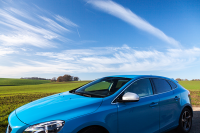 Blue Volvo vehicle driving with green field and blue sky backdrop
