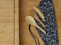 Reusable bamboo cutlery in navy blue cloth wrapping next to a cutting board, a good alternative to plastic