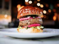 burger with lettuce, red onion, and tomato on a toasted bun with bokeh lights in the background