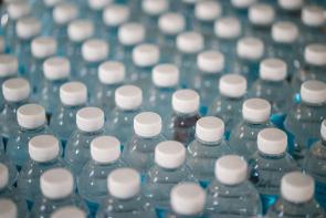 macro shot of rows of clear plastic water bottles with white caps; plastics greenwashing is bad