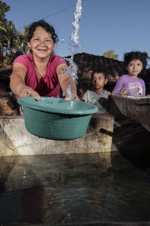 Woman in El Salvador fills bucket of water as her child stands by watching