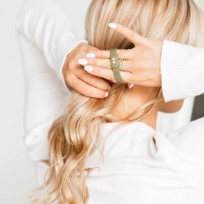 KOOSHOO plastic-free, green hair tie in blond-haired woman's hand, ready to tie into ponytail.
