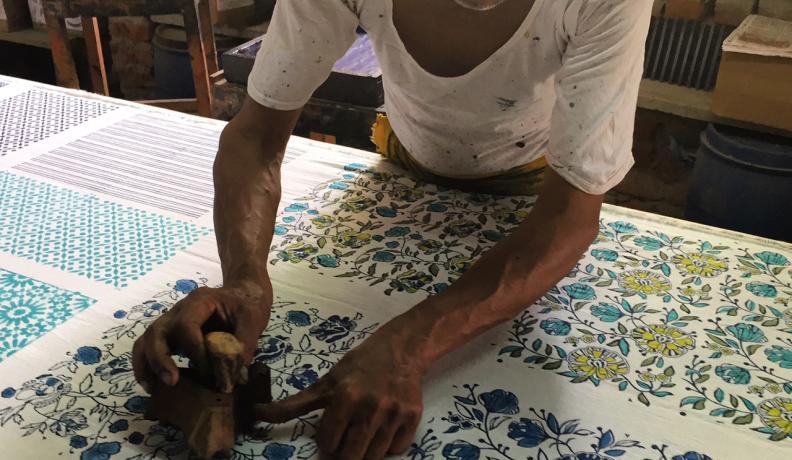 Indian man bends over a piece of cloth and applies a floral wood block print