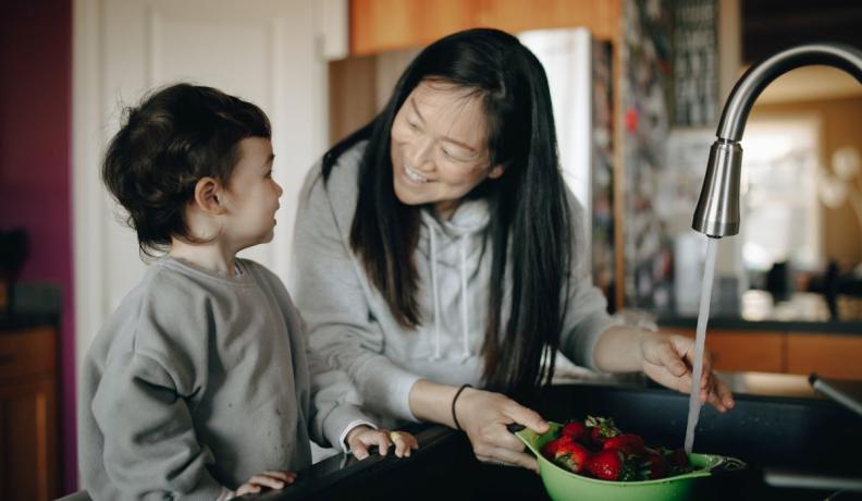 Asian mother and child washing strawberries in the kitchen