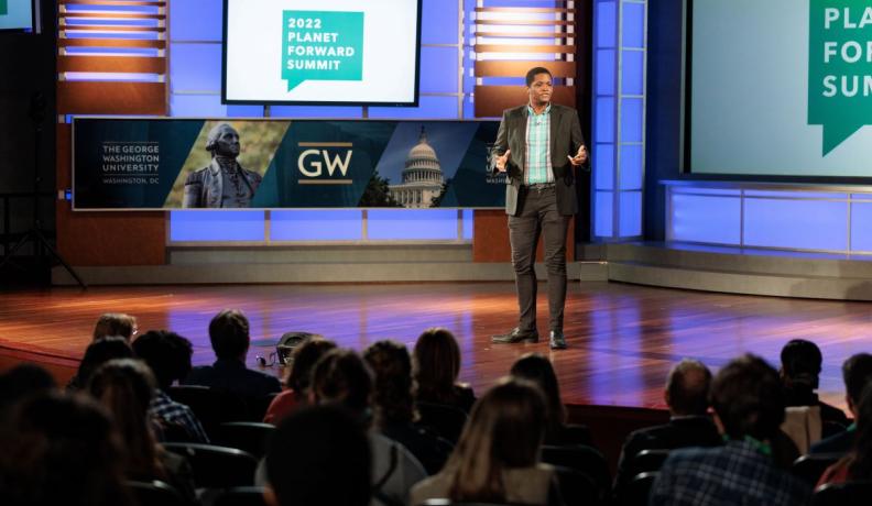Matt Scott in a black suit giving a presentation to an audience at George Washington University's 2022 Planet Forward Summit
