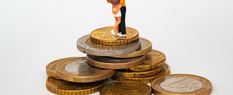 Two clay figures in a romantic embrace stand atop a pile of gold coins. Valentine's Day love money.