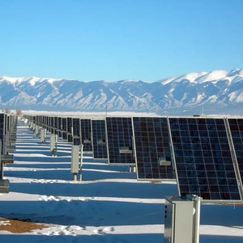 Image: solar panels in a field with snow-capped mountains beyond. Title: Try A Solar Water Heater