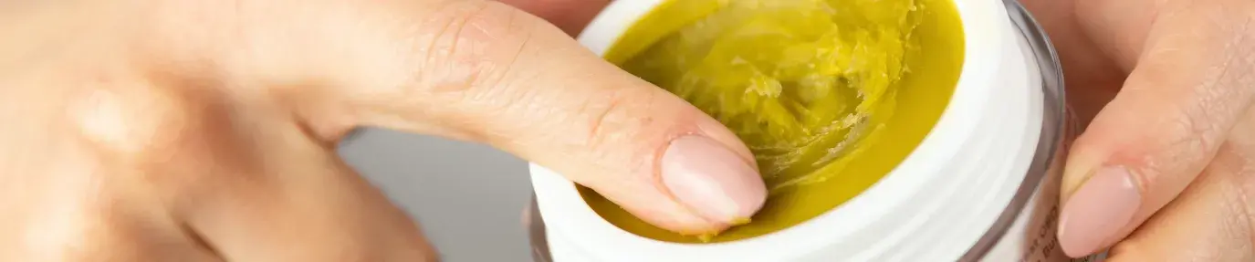 white person rubs their index finger in a yellow balm labeled "Therapeutic CBD skin balm"