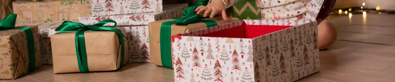 A baby opening Christmas presents in front of a decorated tree. The presents are in boxes and brown paper. Fair Trade Gift Guide.
