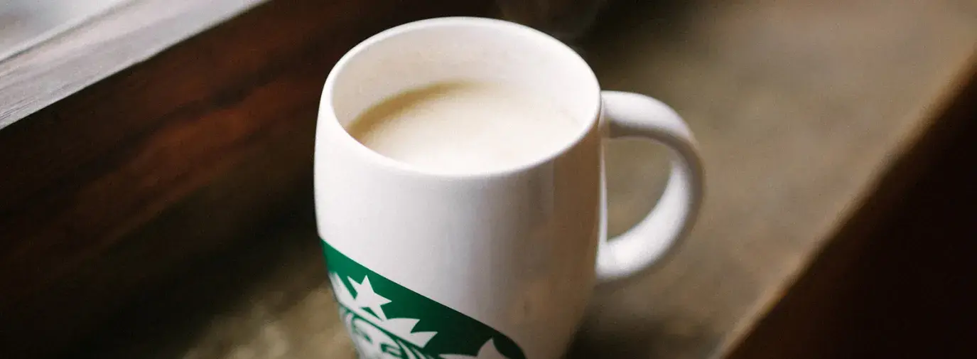 Image: milk in a Starbucks mug. Title: Why is Starbucks’ milk an environmental issue?