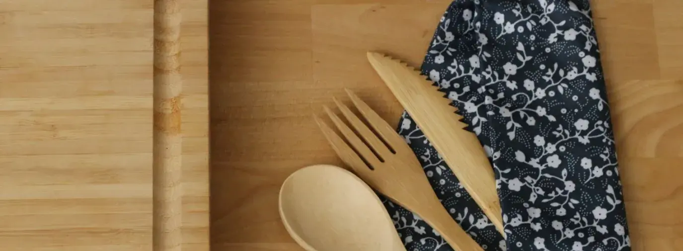 Reusable bamboo cutlery in navy blue cloth wrapping next to a cutting board, a good alternative to plastic
