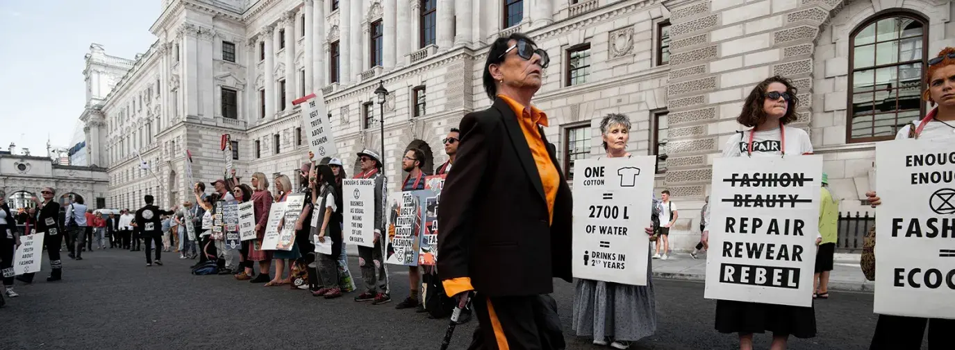 woman in black and yellow outfit walks in front of line of climate protestors from Extinction Rebellion