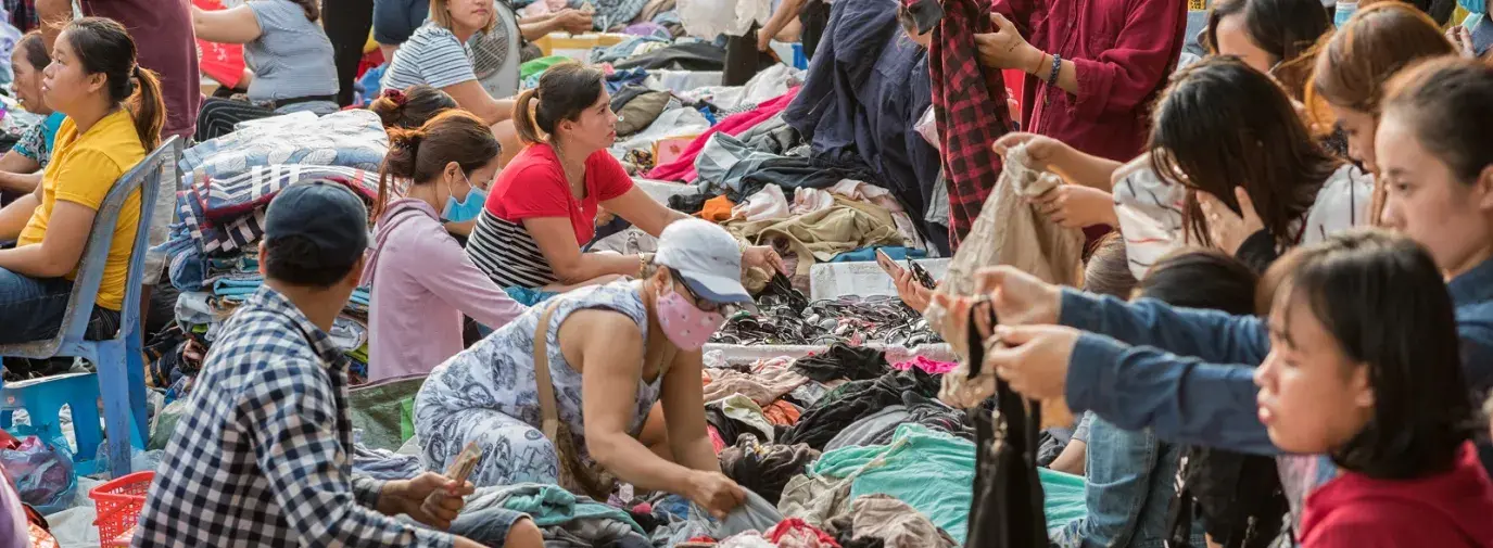 Image: people shop through secondhand clothes at Cho Con Market. Topic: When you donate clothes, they may not go where you think. Learn what really happens to your clothing castoffs.