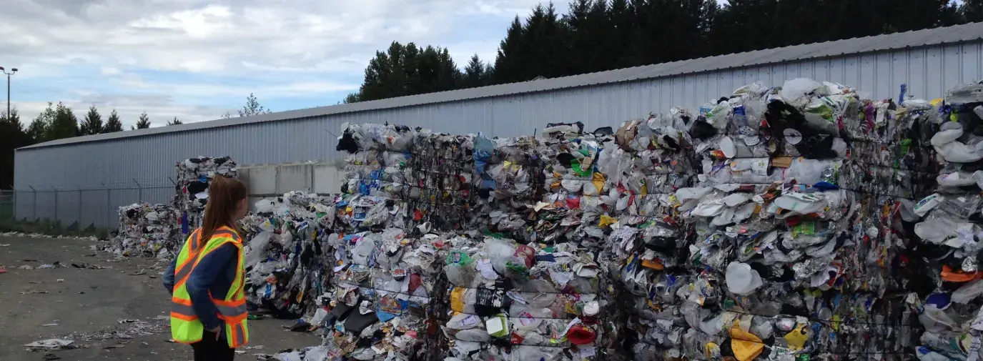 Image: person standing in front of large piles of recyclables. Topic: Does Recycling Help the Climate?