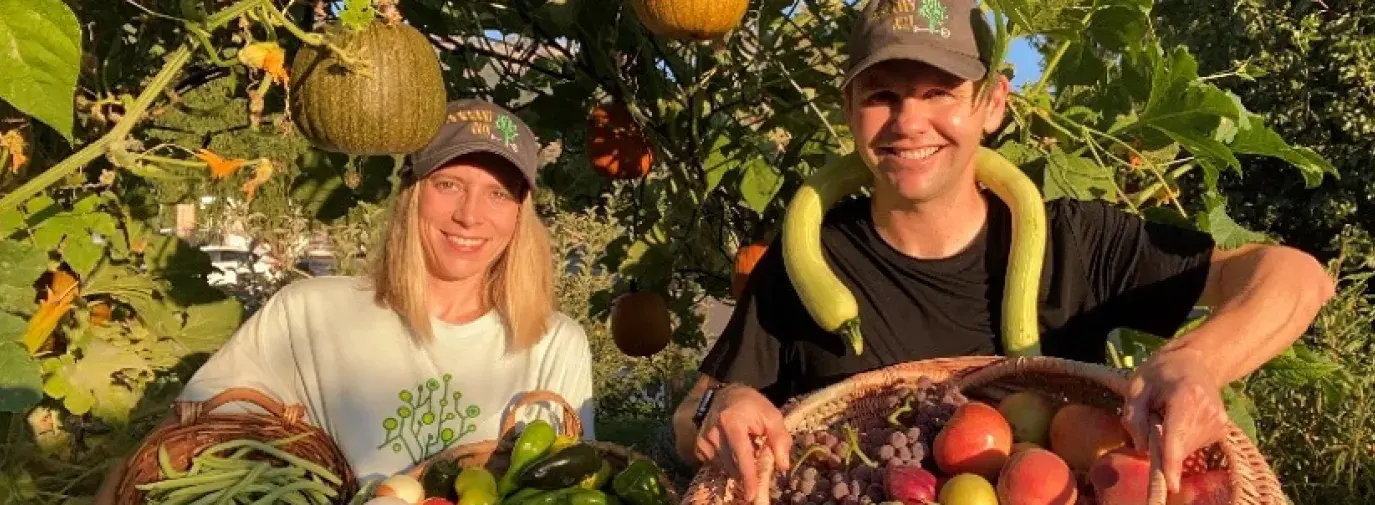 John and Holly in their Climate Victory Garden with baskets of vegetables 