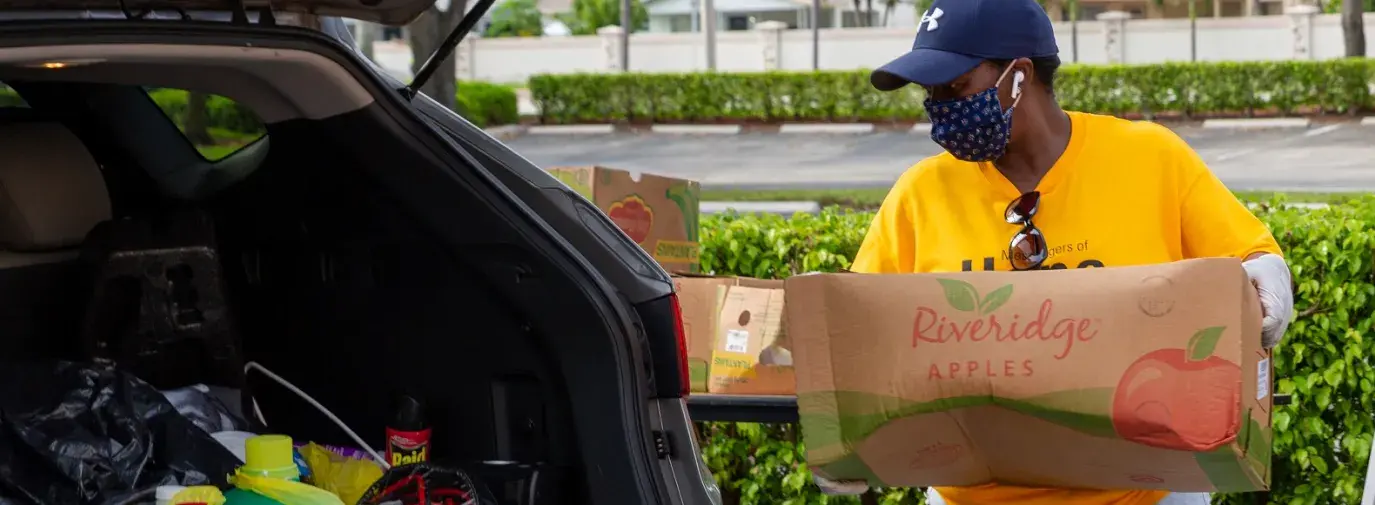 person putting a box of food into the trunk of a car