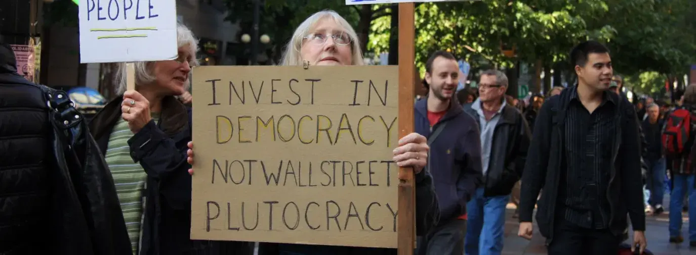 A people's march with signs that read "Invest in democracy, not wall street plutocracy" and "corporations are not people".
