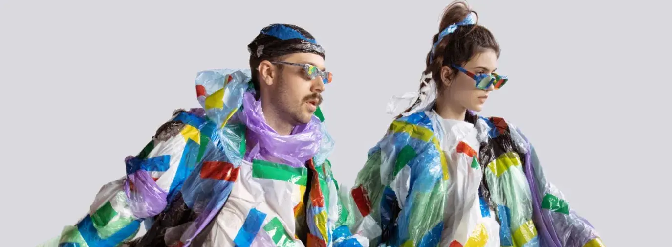 A man and a woman strutting wearing multicolored plastic clothes.