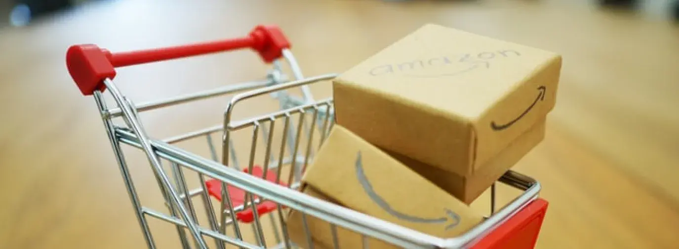 Image: tiny model shopping cart with Amazon boxes. Topic: Amazon Worker Rights: Issues At Home And Abroad
