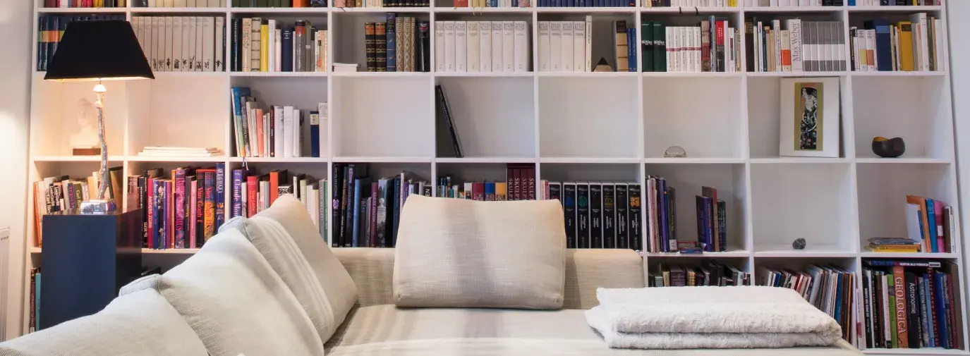 white wooden bookshelves filled with books behind a sectional couch