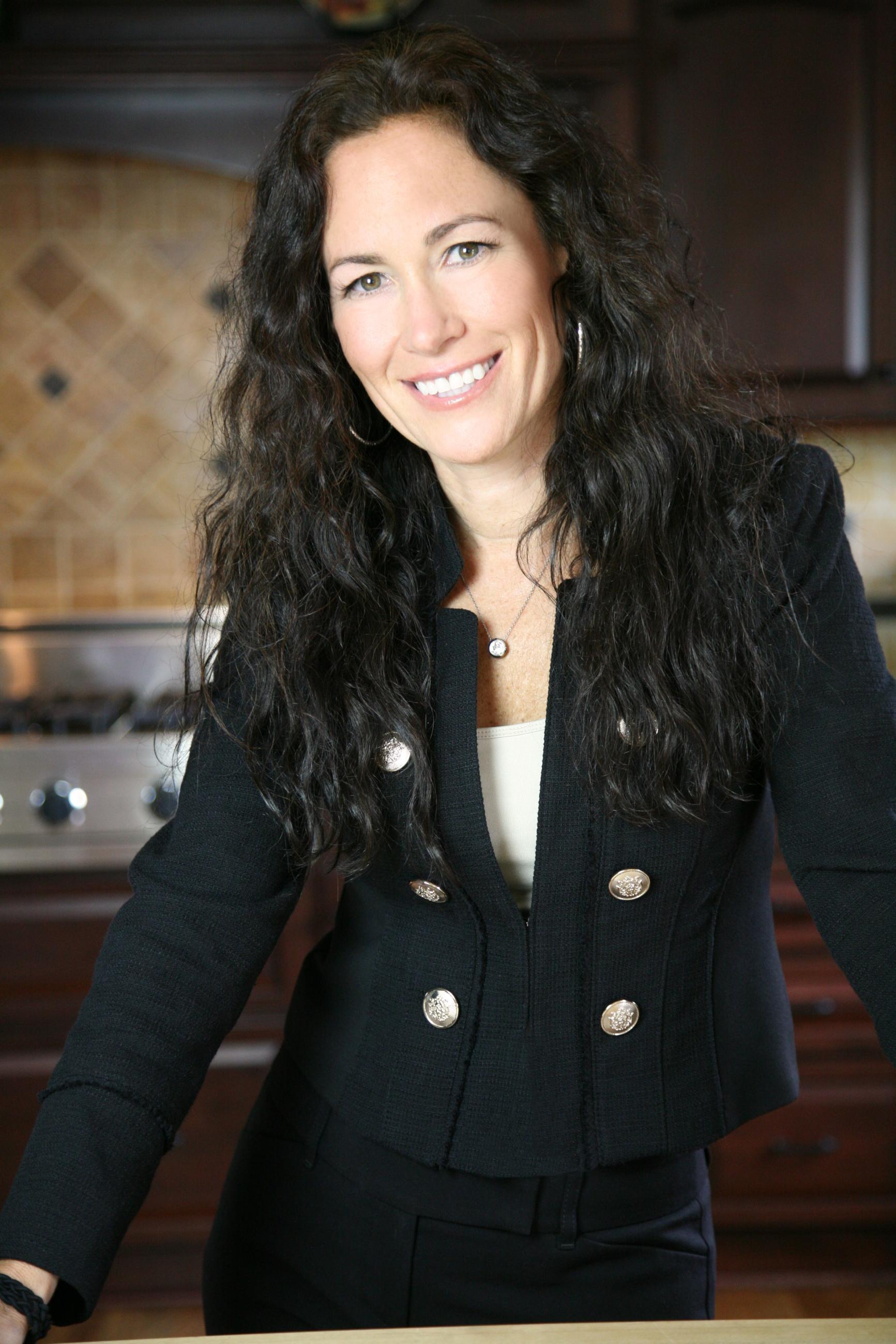 A white woman with long, dark hair wearing a dark blazer in a kitchen. Women Business Owners.