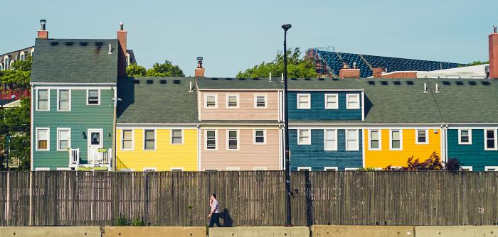 Image: person walking by row of homes. Topic: Green Home.