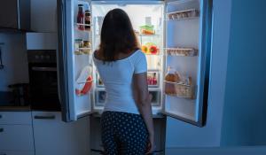 Image: woman looking into open fridge at night. Title: Climate-Friendly Fridges That Are Truly Cool
