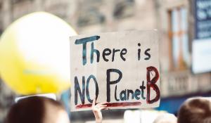 Image: protestor holding sign that says "There is no Planet B." Title: What Do Corporate Commitments for Climate Week Really Mean?