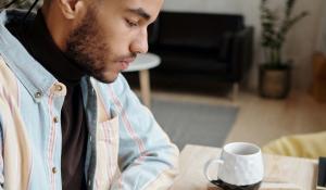 young black man wearing a flannel and studying or working at a desk with a notebook and a cup of coffee.