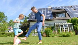 white dad and son playing soccer in the front yard of their house that is covered in solar panels