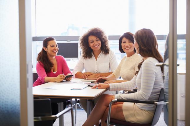 four women sitting around a desk in an office, gender lens investing benefits