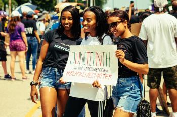 Three young Black women hold a sign that says Juneteenth at a public event